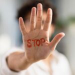 person holding hand up with red writing that reads stop