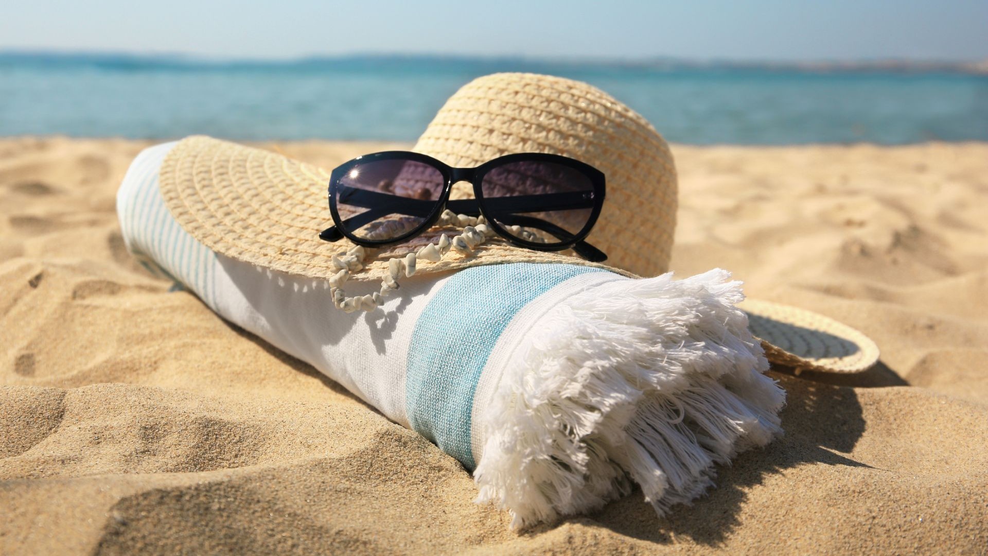 Sun hat, Sunglasses, and beach towel laying on the beach